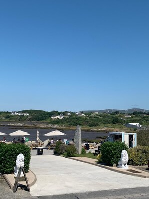 A coastal area with a paved walkway, stone lion statues, and a view of wind turbines in the distance. - Caisleain Oir Hotel (Annagry)