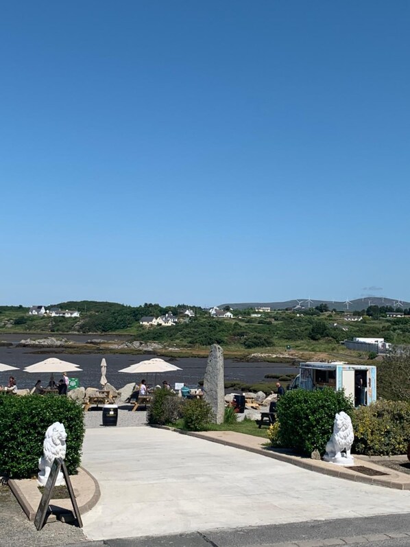 Zona costera con un paseo pavimentado, estatuas de leones de piedra y vistas de aerogeneradores a lo lejos.