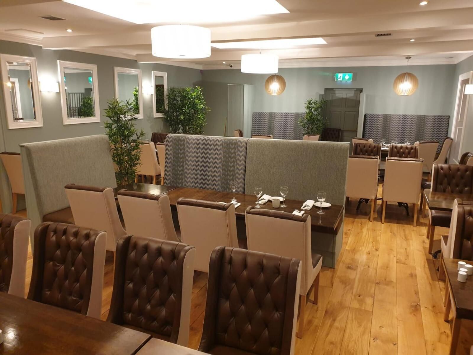 A restaurant with booths and tables, wooden flooring, and pendant lighting.