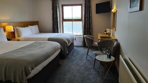 Une chambre d’hôtel avec deux lits, un bureau avec une chaise, une télévision et une vue sur la mer par la fenêtre.