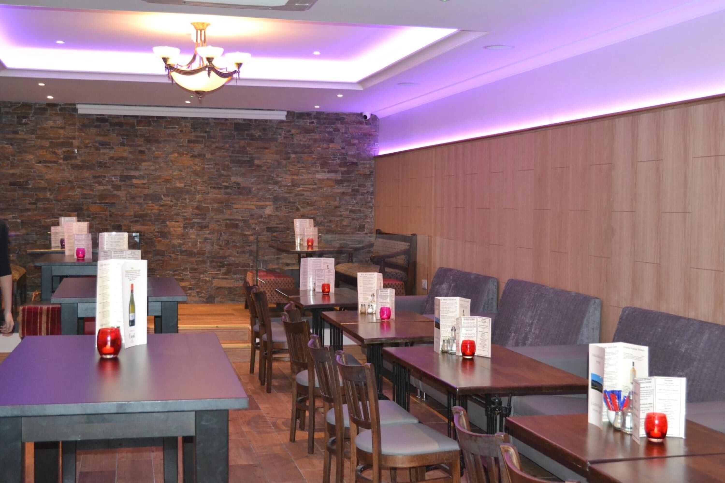 A restaurant with wooden tables and chairs, stone walls, and purple ambient lighting.