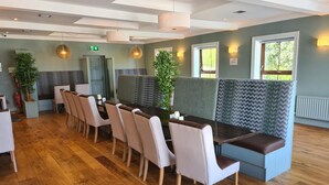 Un espace repas comprenant une longue table, plusieurs chaises et un coin salon avec des fauteuils à dossier décoré.