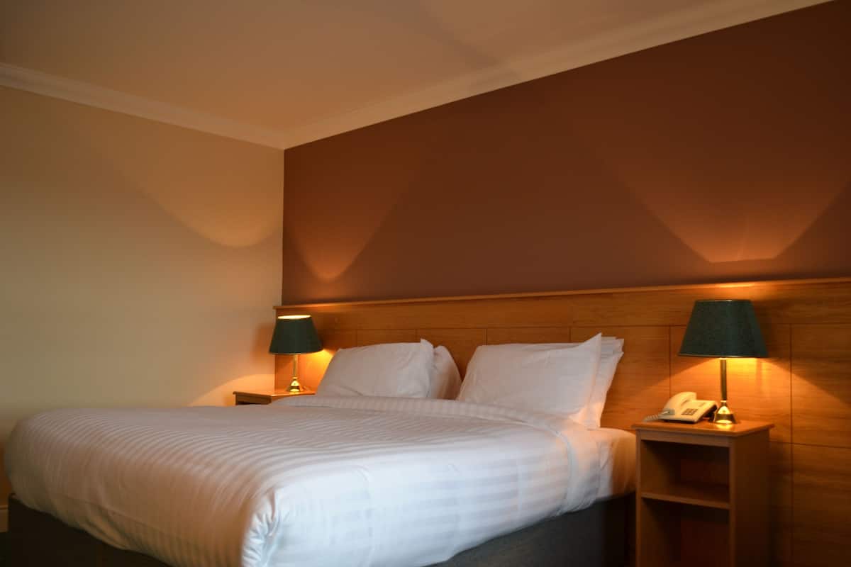 Ein Hotelzimmer mit einem großen Bett, zwei Nachttischen mit Lampen und einem Holzkopfteil.