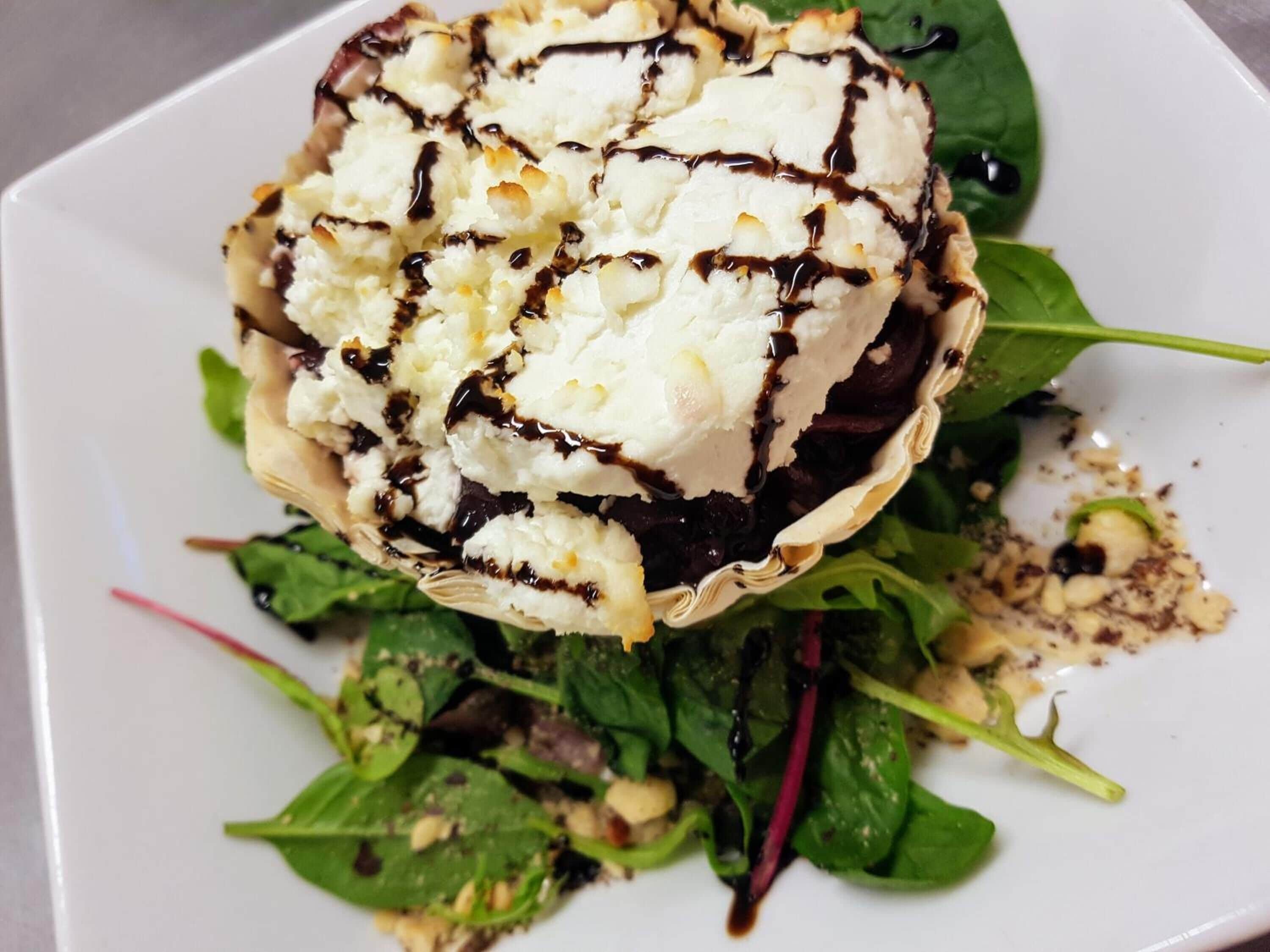 A dessert consisting of a scoop of ice cream with chocolate drizzle on a bed of greens.