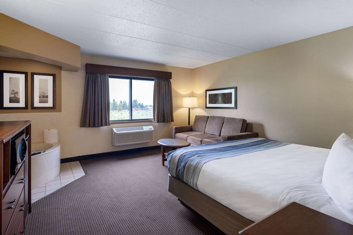Une chambre d’hôtel avec un grand lit, un canapé, une petite table, un bureau, une chaise, une lampe et une fenêtre avec des rideaux.