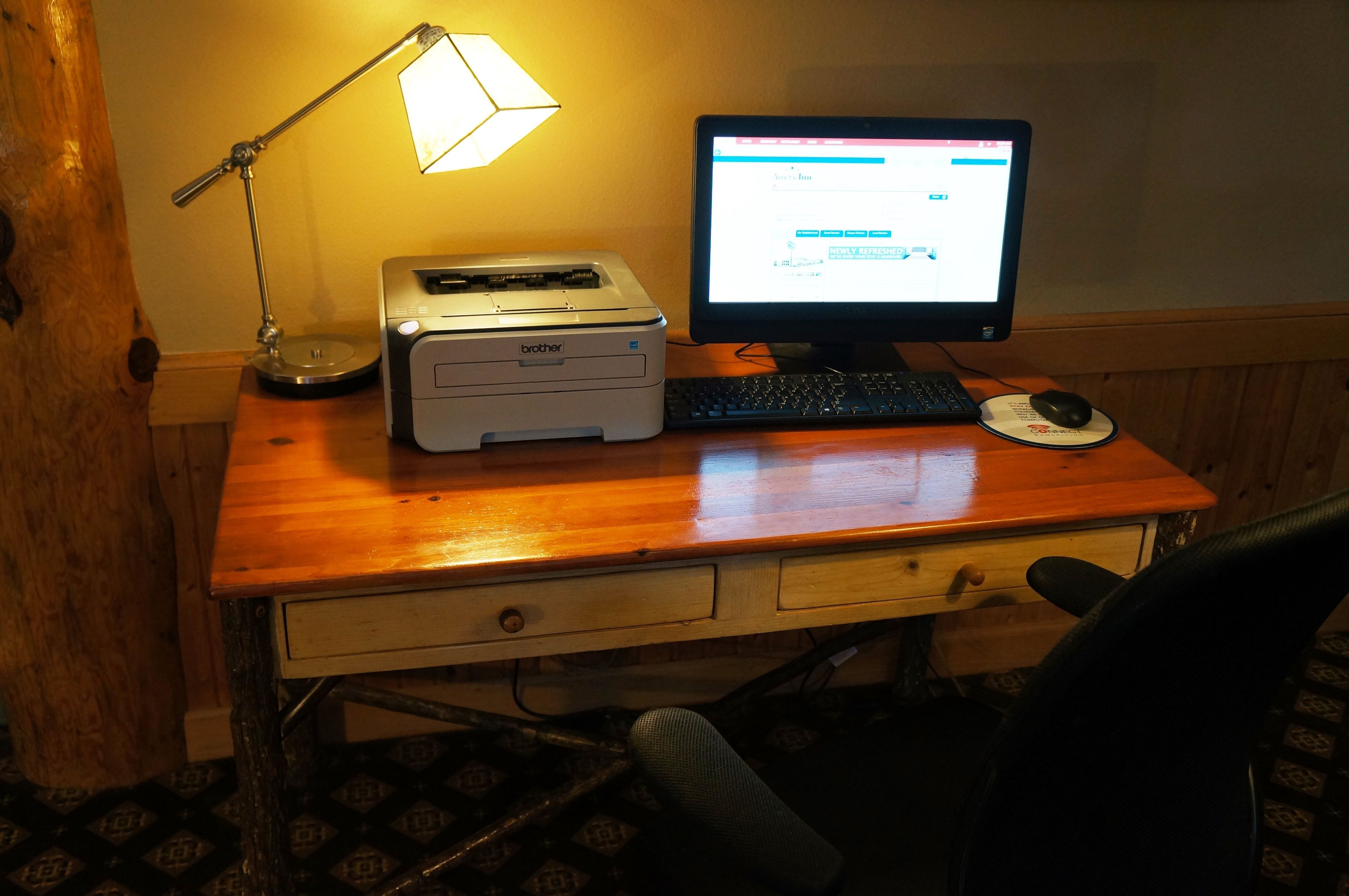 Un escritorio de madera con una impresora Brother, un monitor de computadora, un teclado y un ratón.