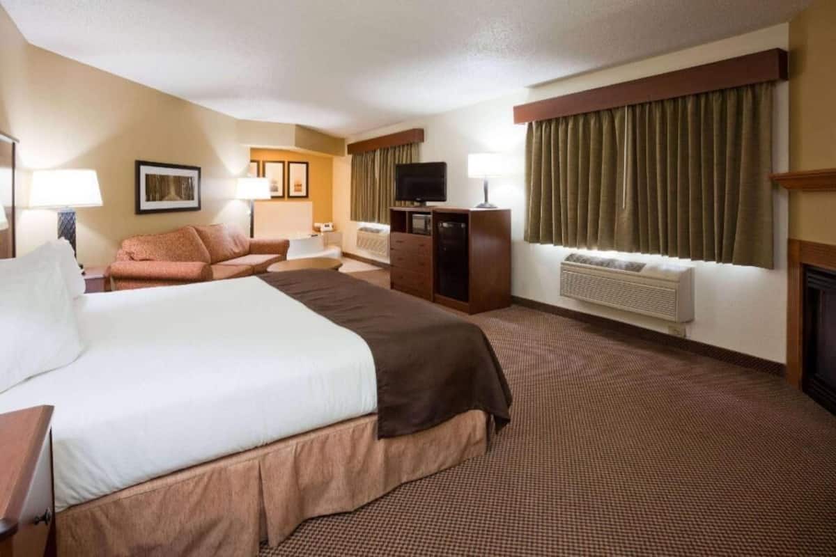 A hotel room with a large bed, a desk, a television, and a fireplace.