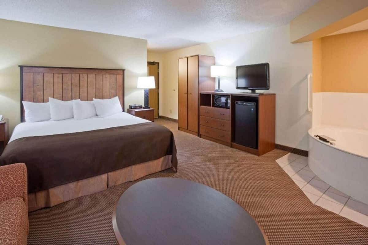 A hotel room with a bed, a desk with a television, a minibar, and a bathtub.