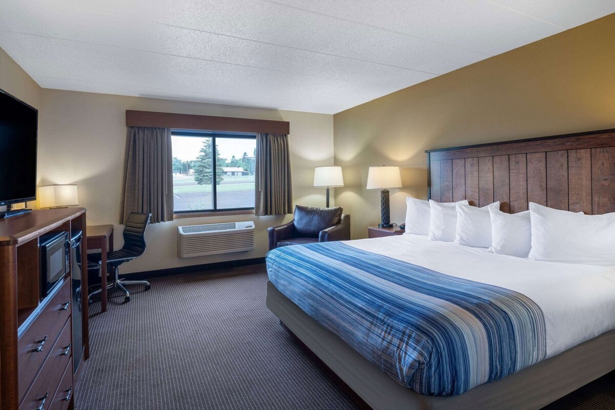 Een hotelkamer met een bed, een bureau, een stoel, een televisie en een raam met gordijnen.