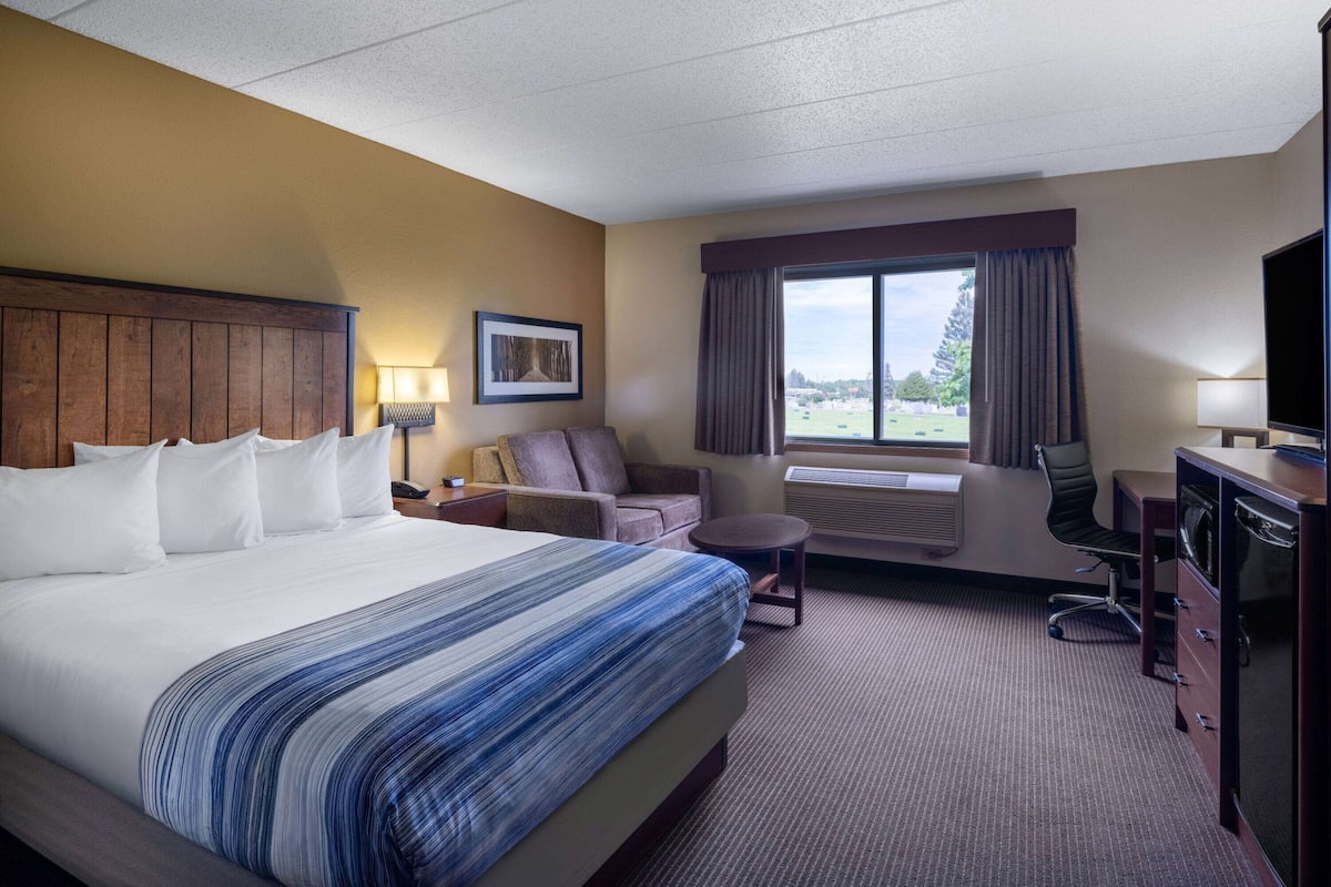 Une chambre d’hôtel avec un grand lit, un bureau, une chaise, un canapé et une fenêtre donnant sur un beau paysage.
