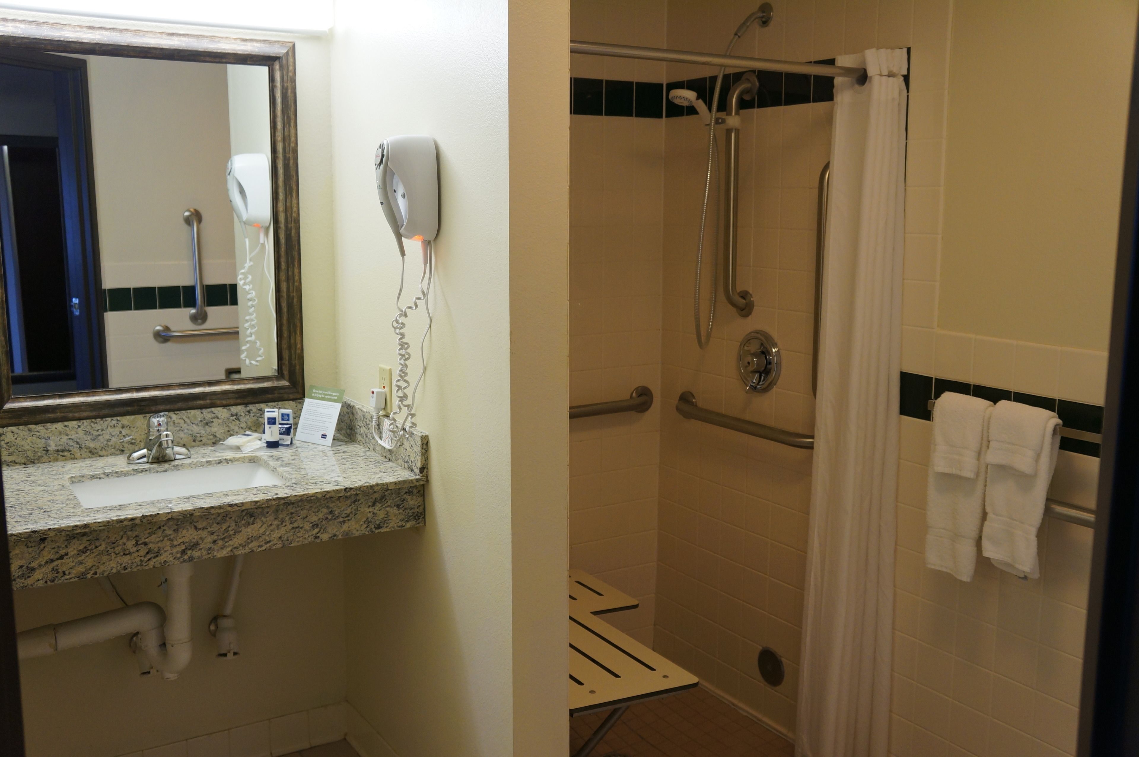 Une salle de bain équipée d’un lavabo, d’un miroir, d’un sèche-cheveux et d’une douche avec des barres d’appui.