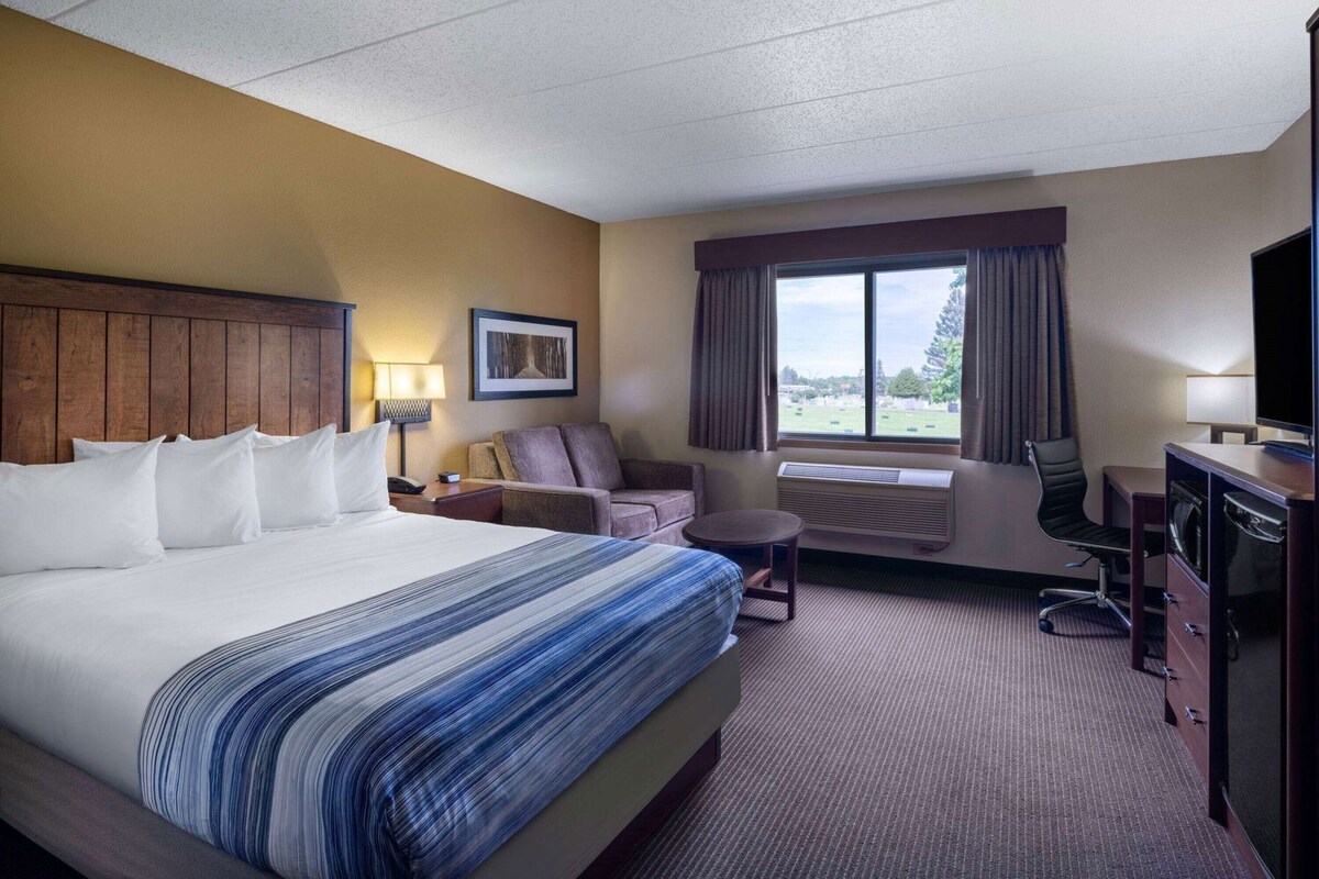 Een hotelkamer met een groot bed, een bureau met stoel, een bank en een raam met gordijnen.