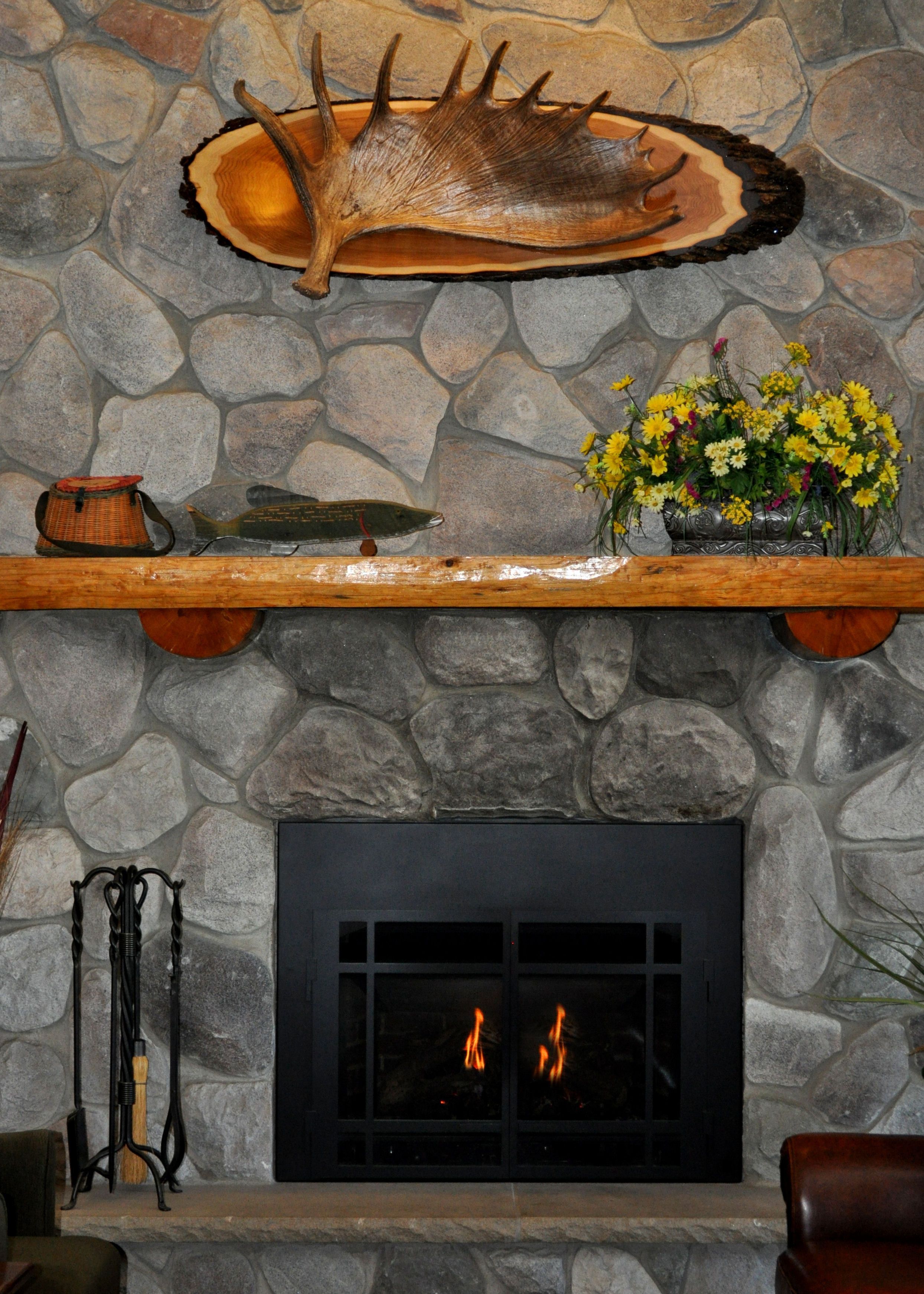 Una chimenea de piedra con un tronco de madera, un estante con adornos y un jarrón con flores.
