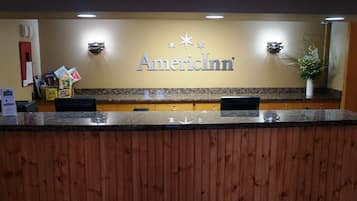 A reception desk with a wooden counter, a sign reading "AmericInn", and a wall-mounted information board.