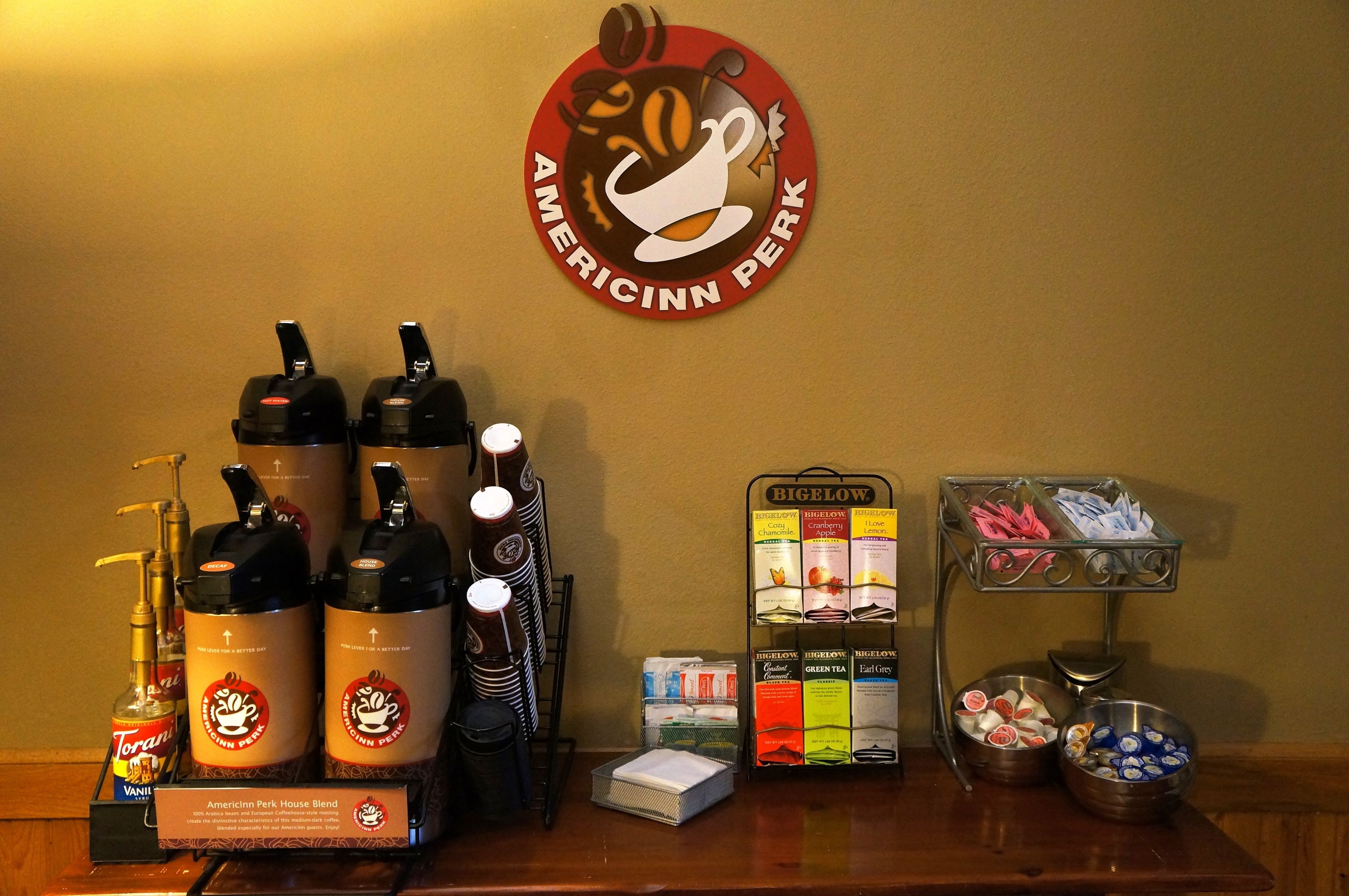 A coffee station with Torani syrup bottles, Americinnn perk branded coffee dispensers, and Bigelow tea boxes.