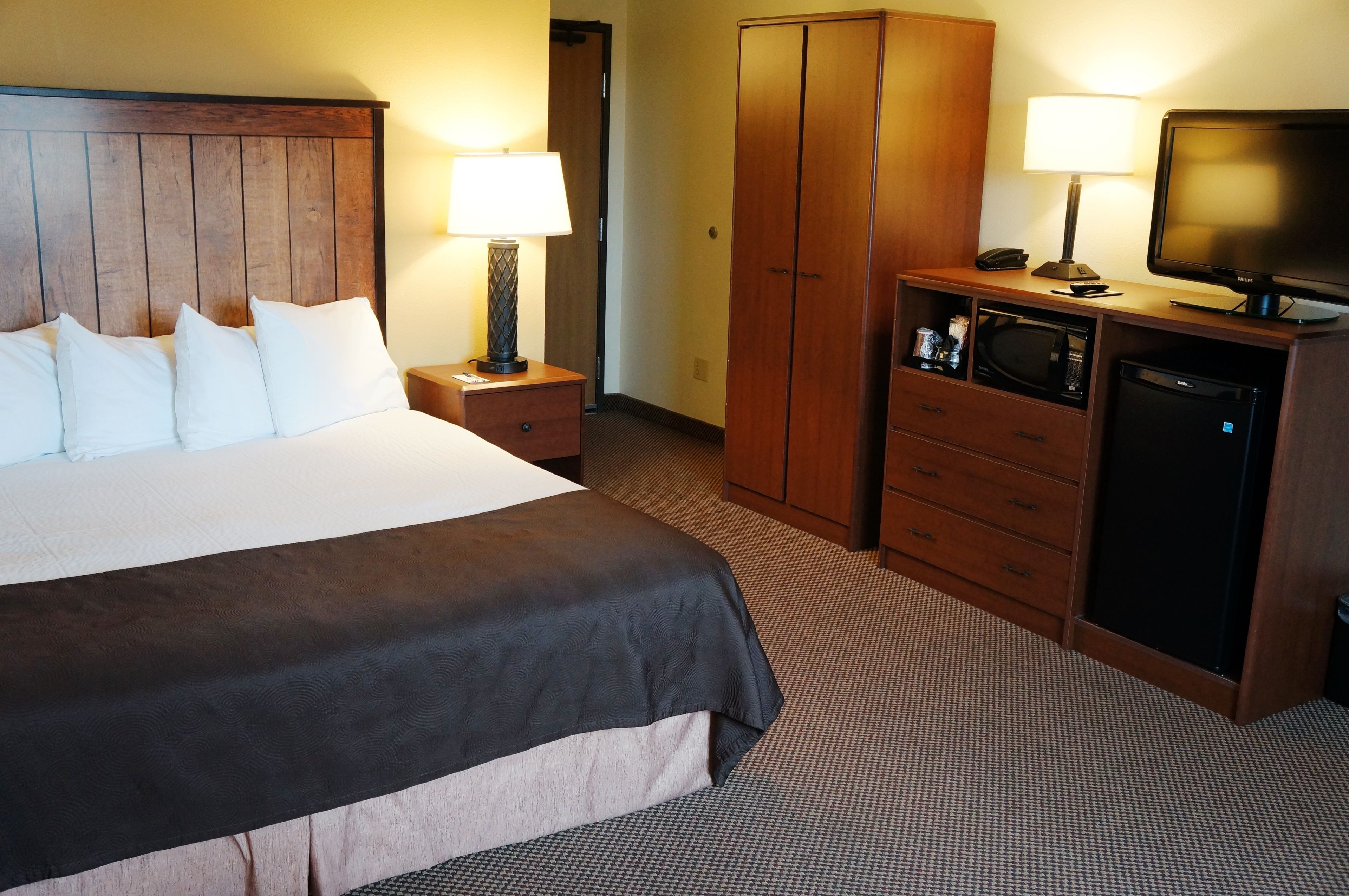 Ein Hotelzimmer mit einem großen Bett, einem Holzschrank, einem Schreibtisch mit Lampe, einem Fernseher und einer Mikrowelle.