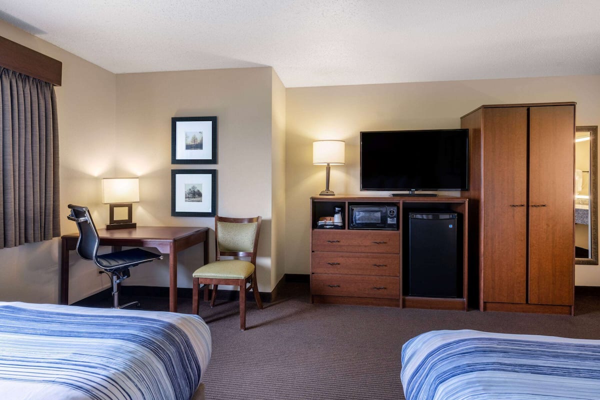 Une chambre d’hôtel avec deux lits, un bureau avec une chaise, une télévision, un réfrigérateur et une armoire.