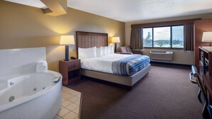 Une chambre d’hôtel avec un grand lit, une salle de bain séparée avec une baignoire, une fenêtre avec vue et un bureau avec une lampe.