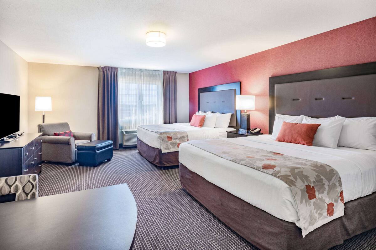 Quarto de hotel com duas camas, uma escrivaninha, uma cadeira e uma televisão.