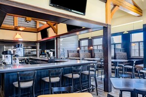 A restaurant with a bar area, seating, and a kitchen in the background. - Hawthorn Suites by Wyndham Williston (Williston)