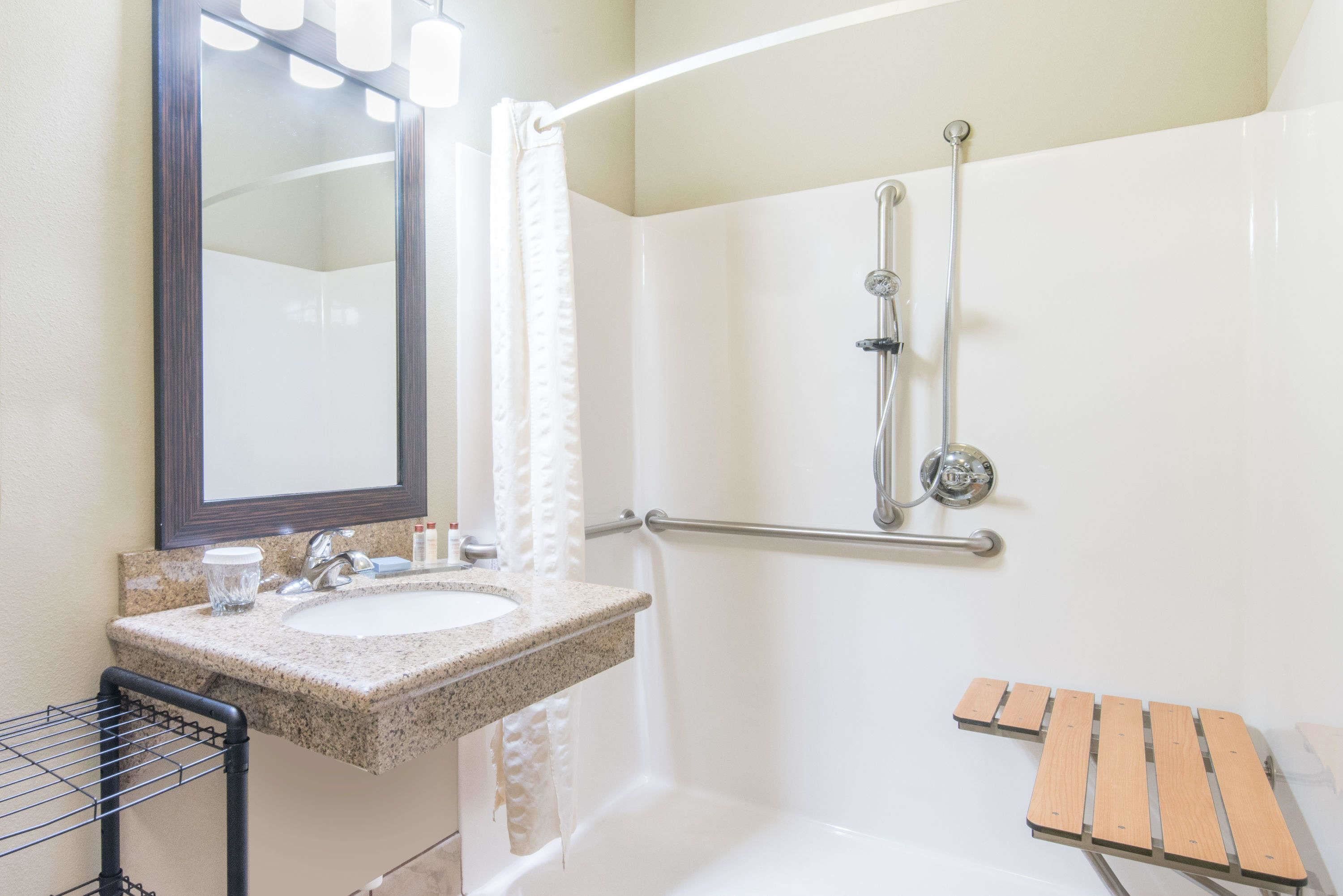 A bathroom with a sink, mirror, shower, and a wooden bench.