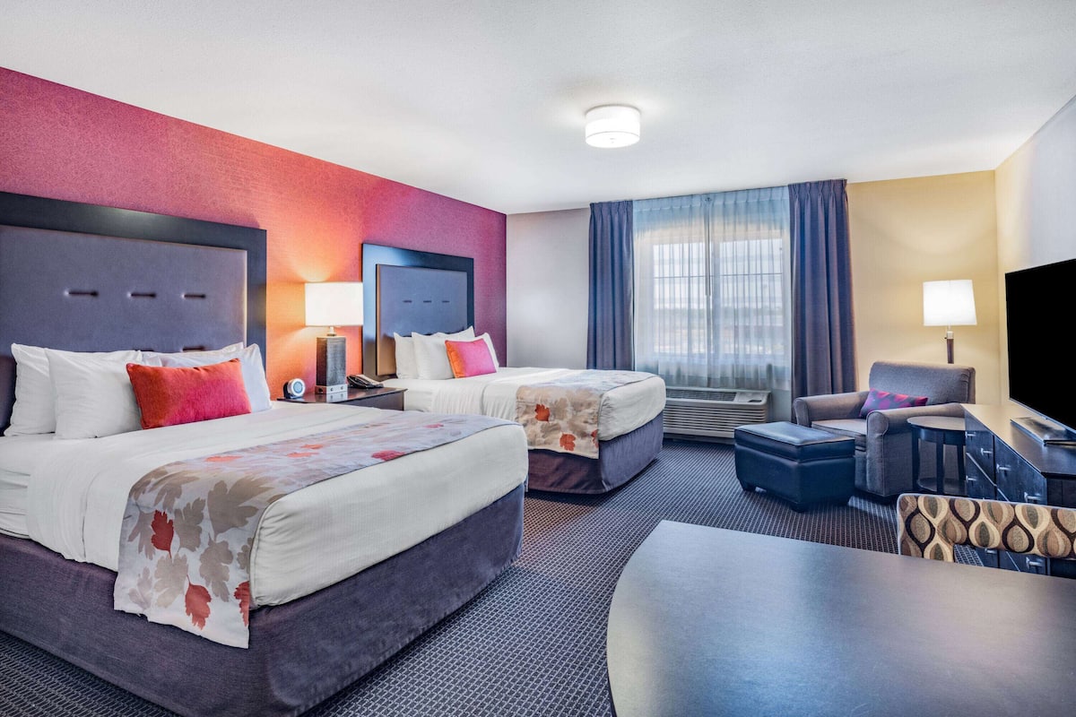Quarto de hotel com duas camas, uma escrivaninha, uma cadeira e uma televisão.