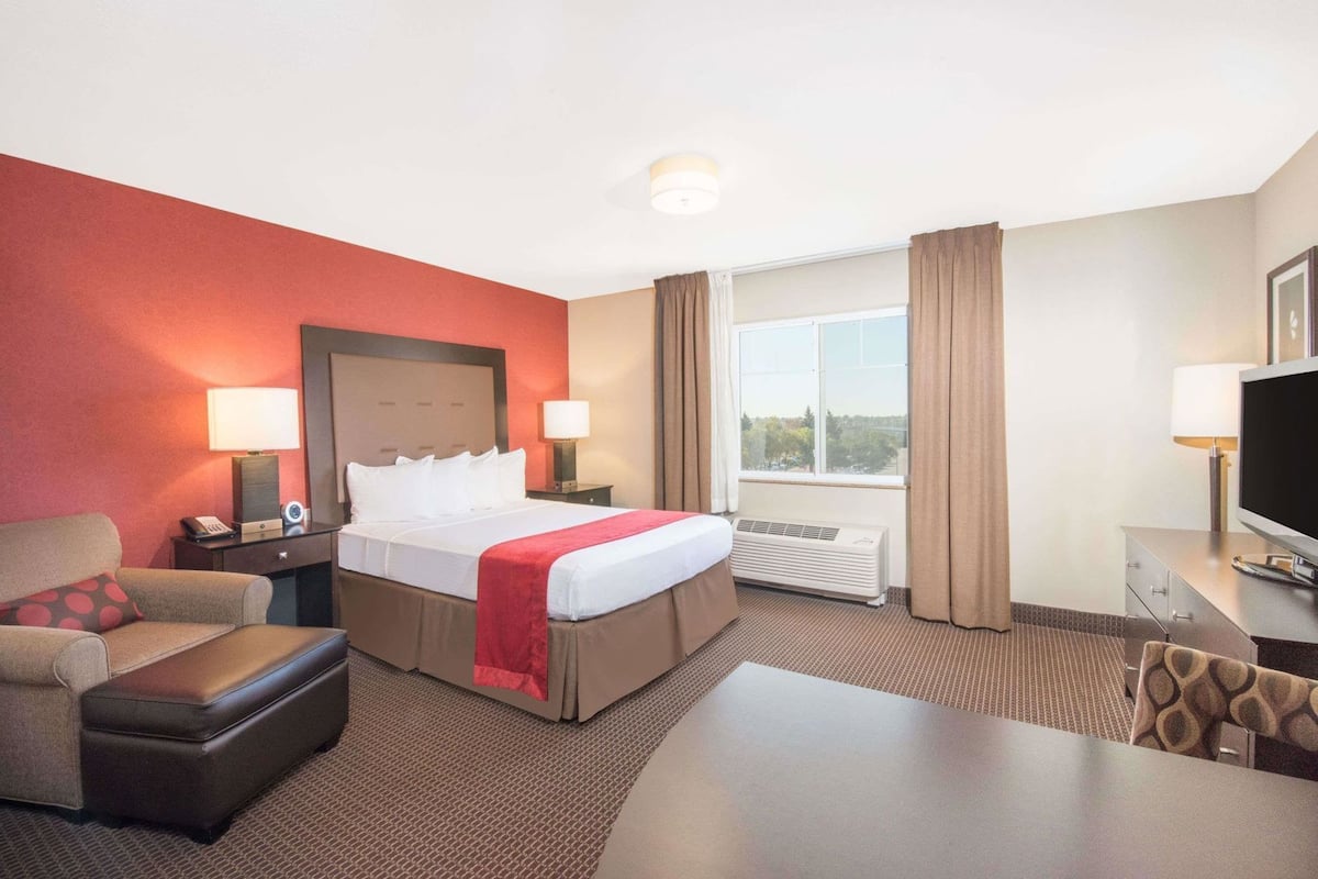 Quarto de hotel com cama, escrivaninha, cadeira, televisão e janela.