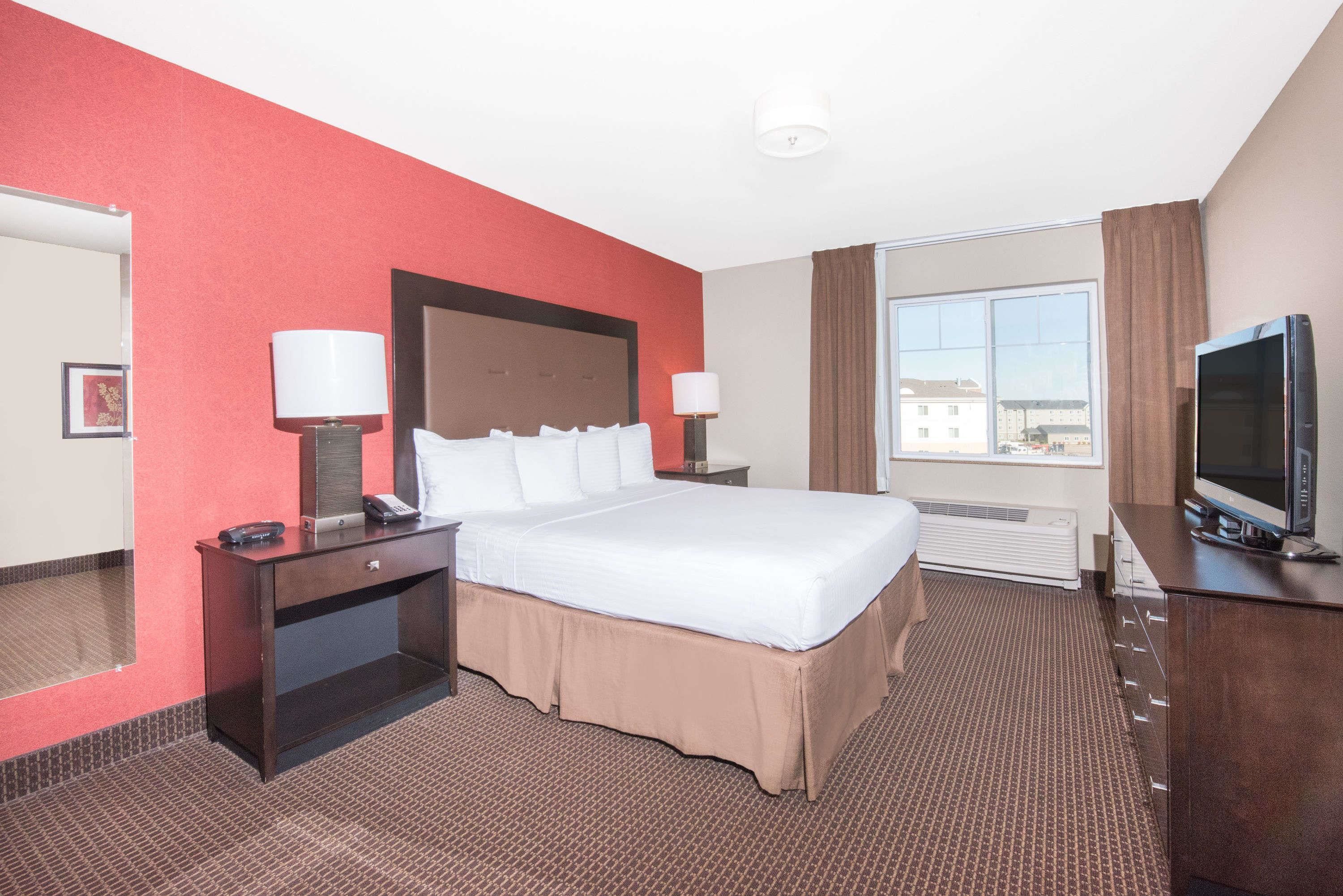 A hotel room with a large bed, two bedside tables with lamps, a TV, and a window with curtains.