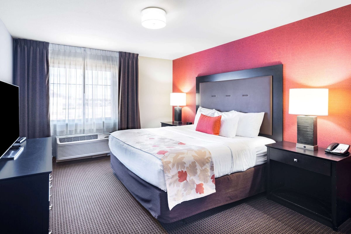 Quarto de hotel com uma cama grande, duas mesas de cabeceira com abajures, uma TV de tela plana e uma janela com cortinas.