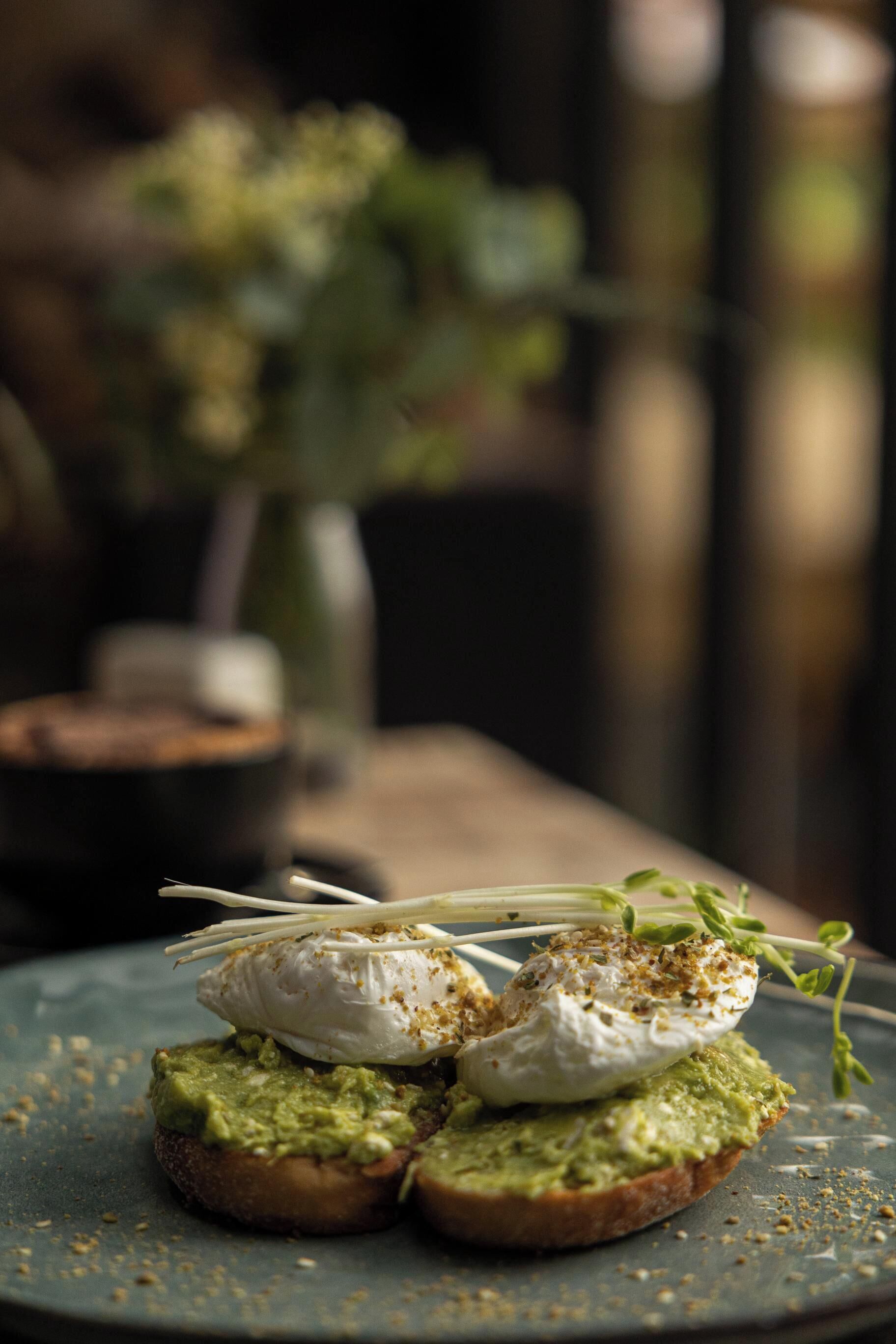 A plate with avocado toast topped with poached eggs and herbs.