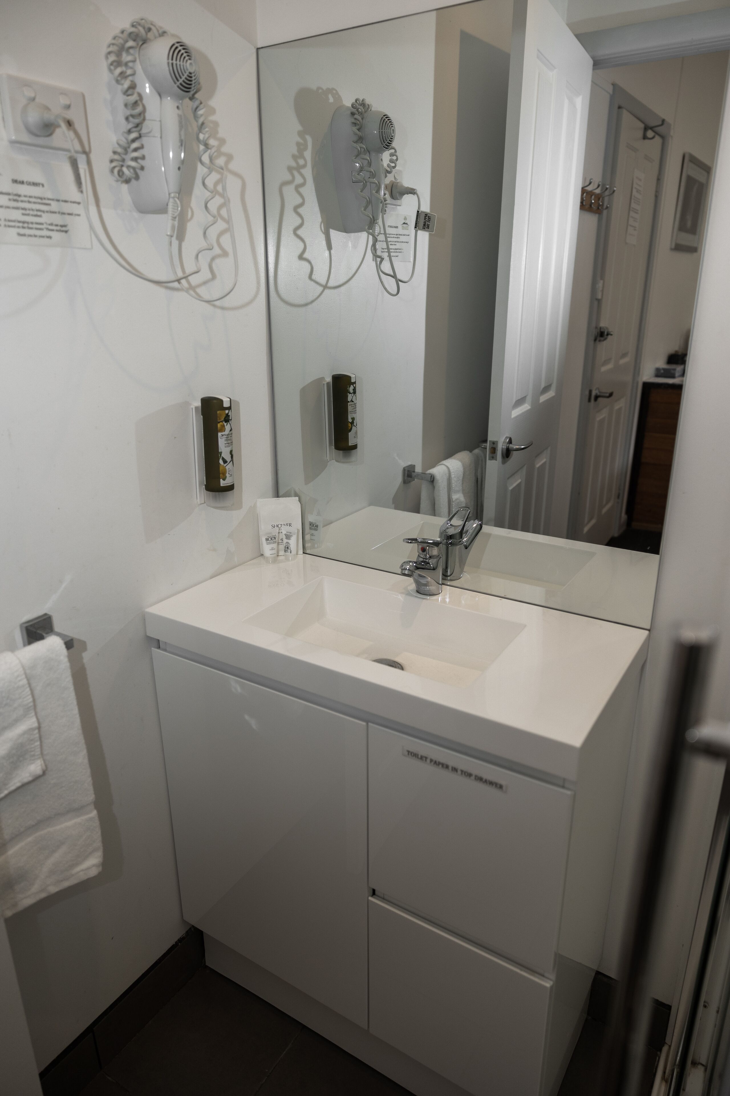 A bathroom with two sinks, a mirror, and a hairdryer mounted on the wall.