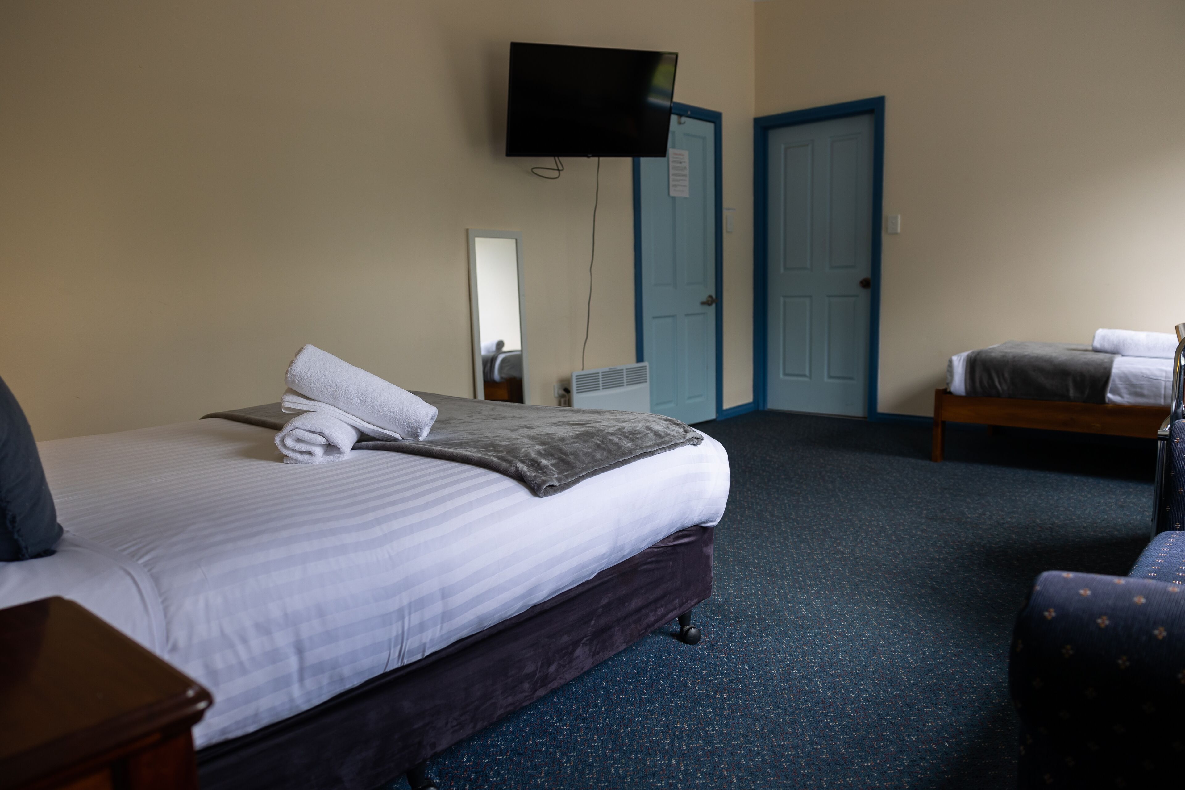 A hotel room with a bed, a TV, a mirror, a door, and a small table.