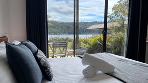Een hotelkamer met een bed, uitzicht op een meer en een stoel buiten.