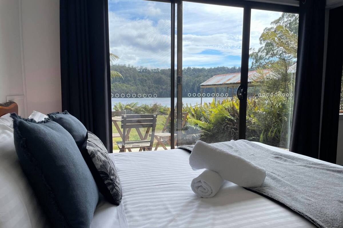 A hotel room with a bed, a view of a lake, and a chair outside.