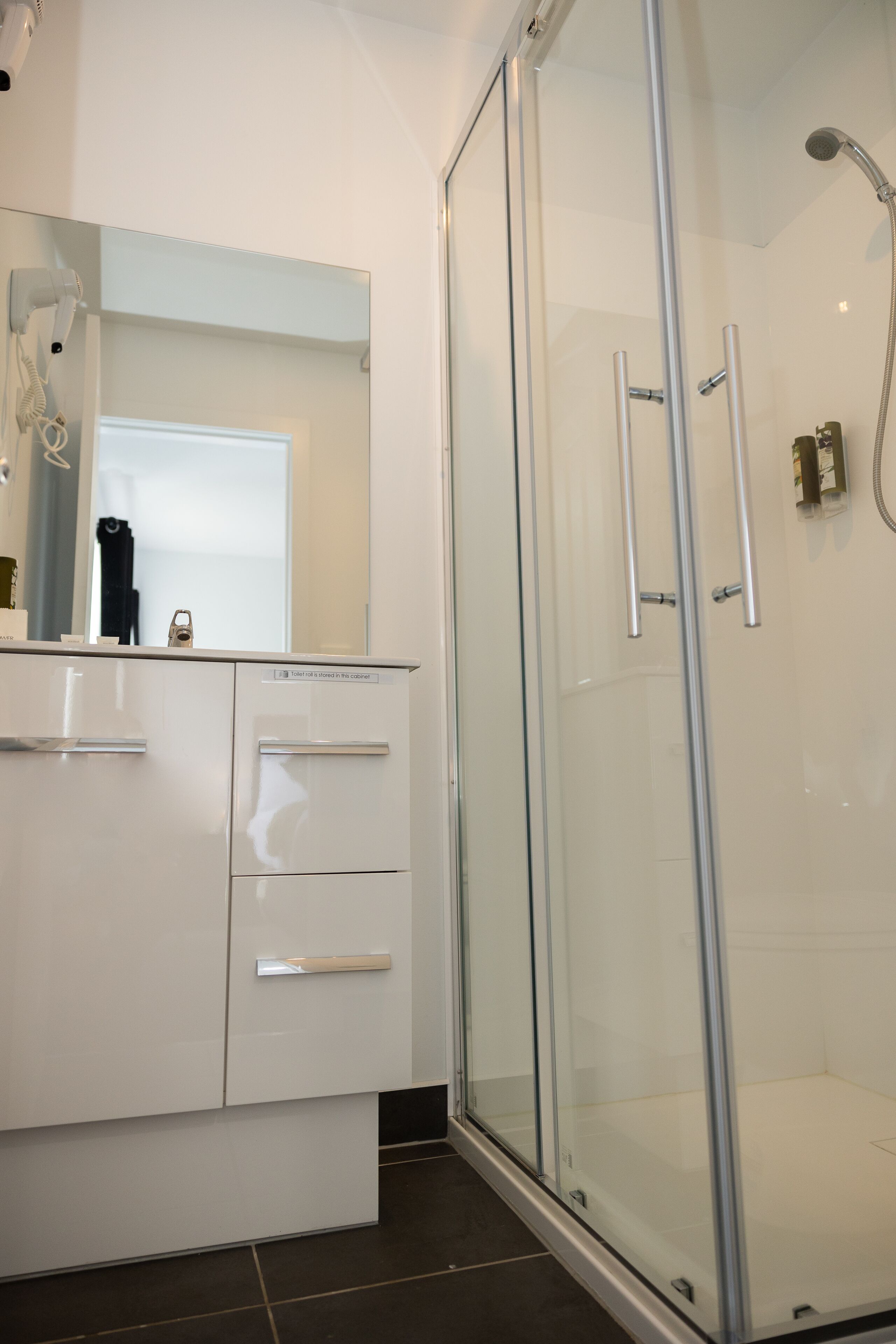 A modern bathroom with a glass shower enclosure, a white vanity with drawers, and a large mirror.