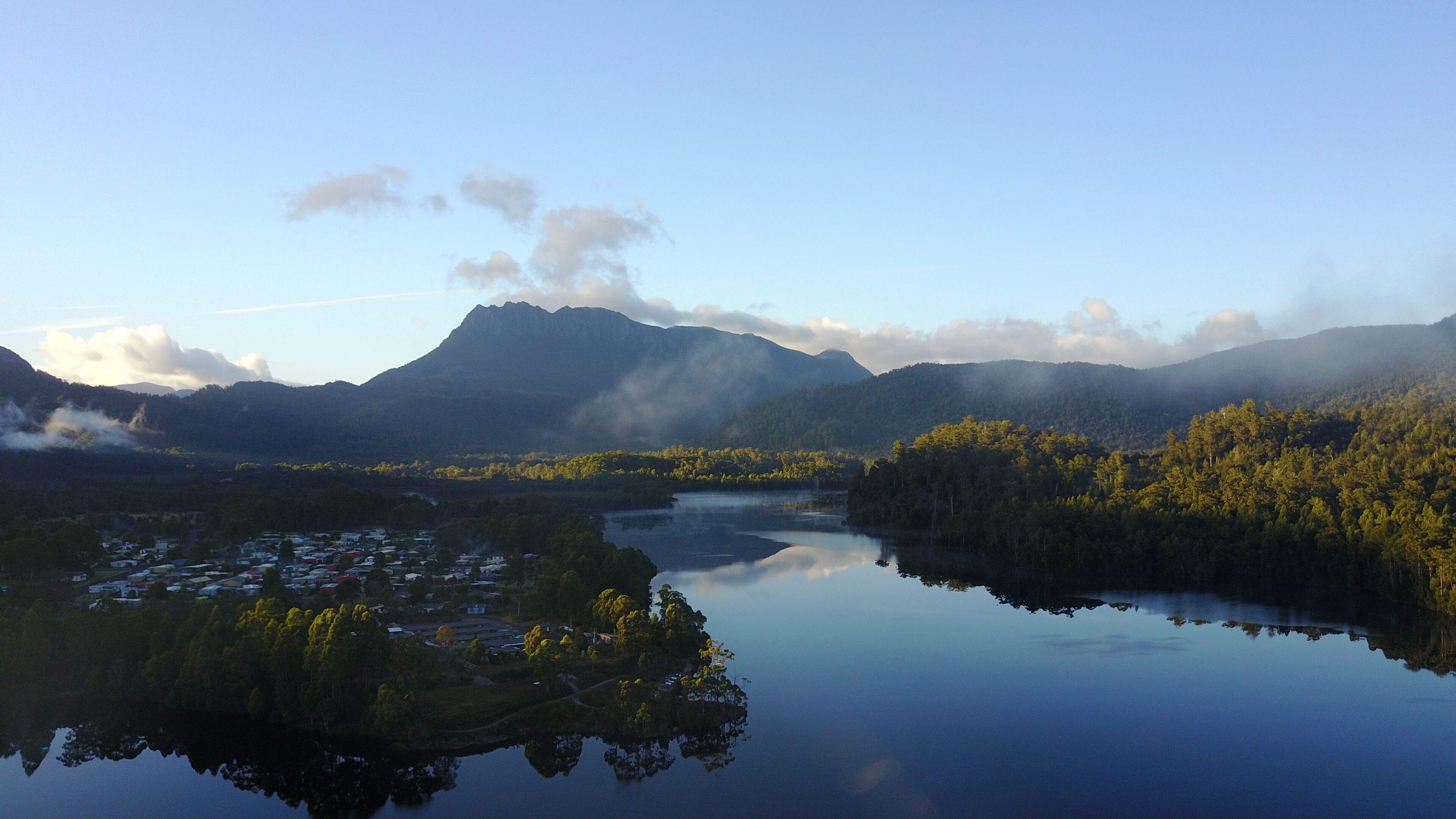 A calm lake reflecting the surrounding forest and mountains.
