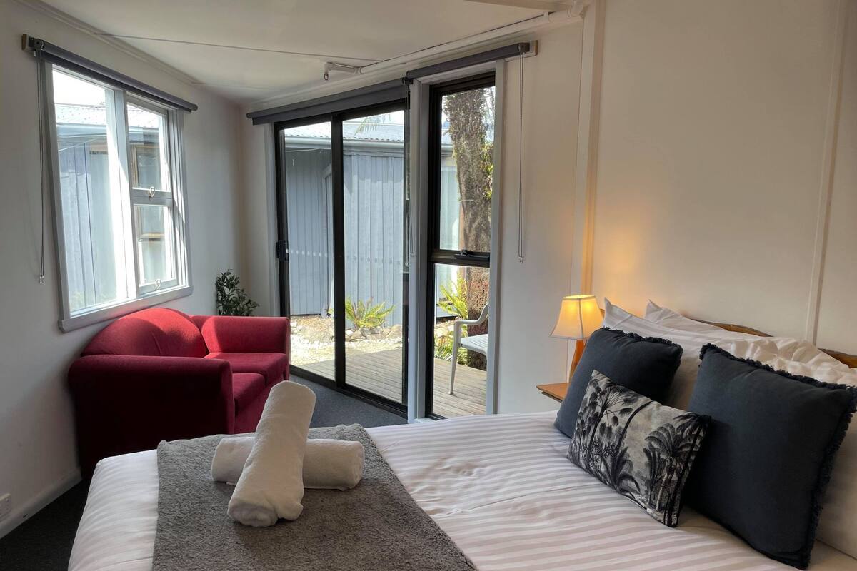 A hotel room with a bed, a red chair, a large window, and a view of the outdoors.