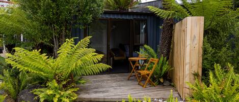 A wooden deck with a table and chairs, surrounded by lush greenery and ferns.