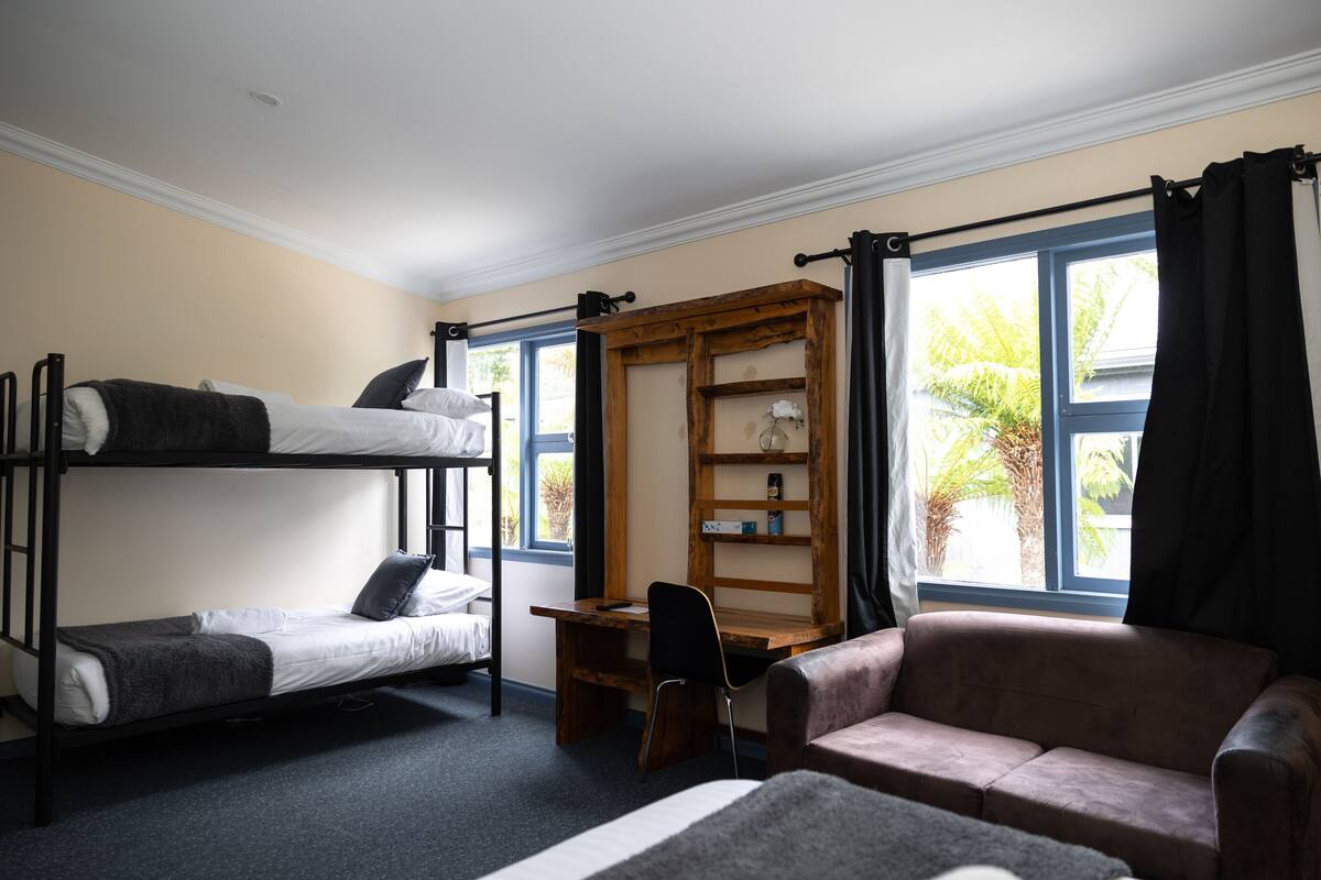 A dorm-style room with bunk beds, a desk, a chair, and a sofa.
