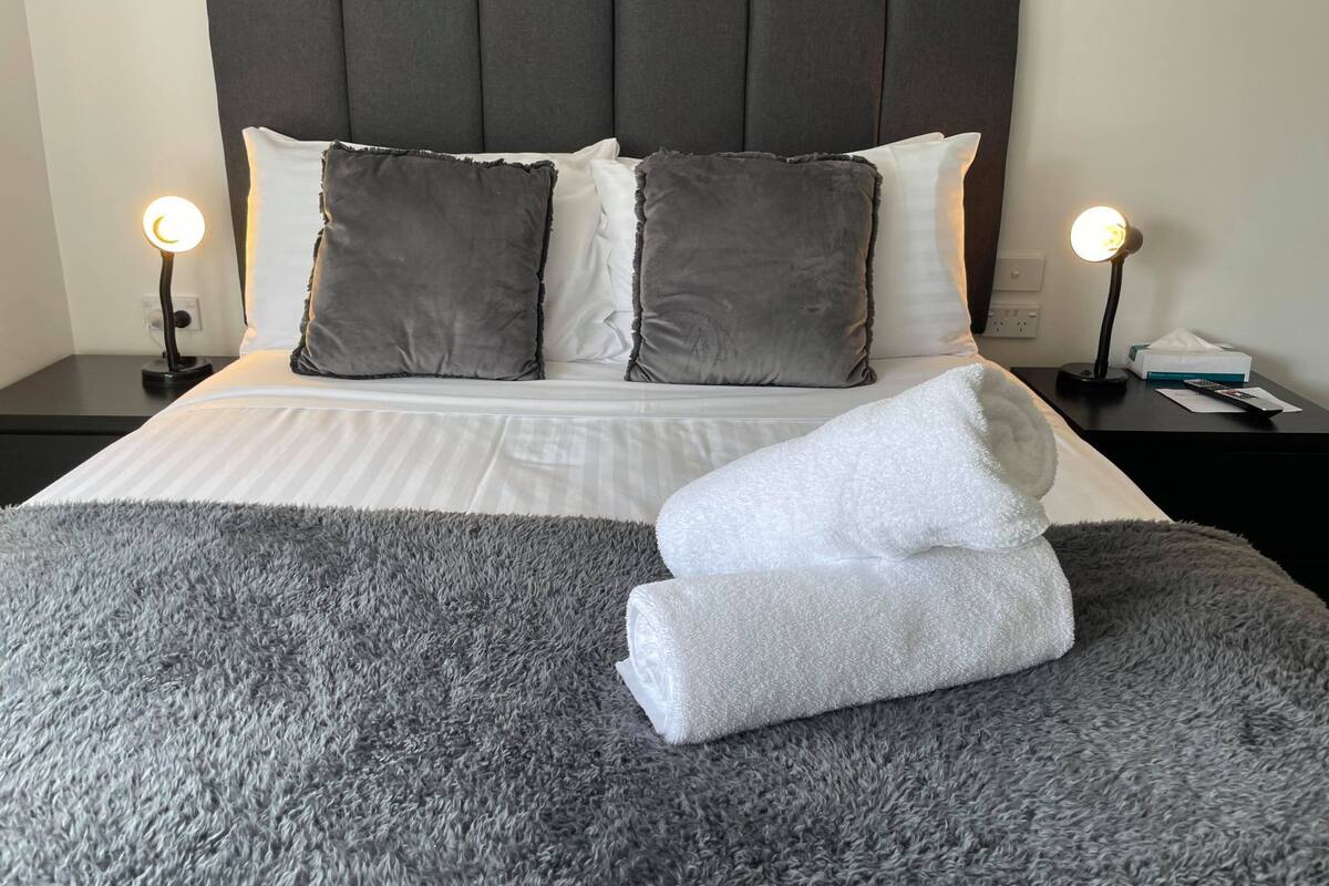 A neatly made bed with a grey fluffy blanket, two bedside lamps, and a grey headboard.