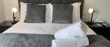 A neatly made bed with a grey fluffy blanket, two bedside lamps, and a grey headboard.