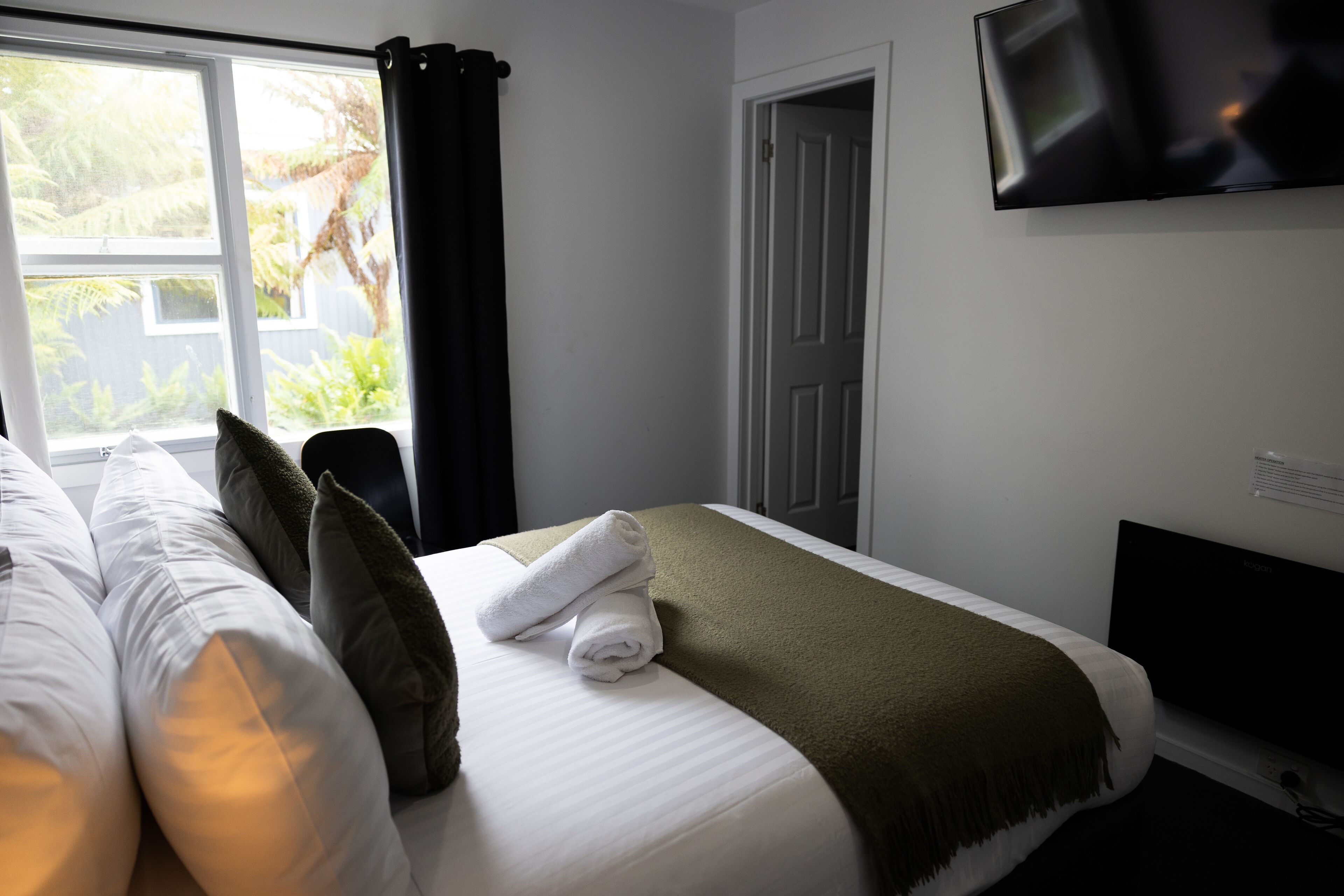 Una habitación de hotel con cama, televisión y ventana con cortinas.