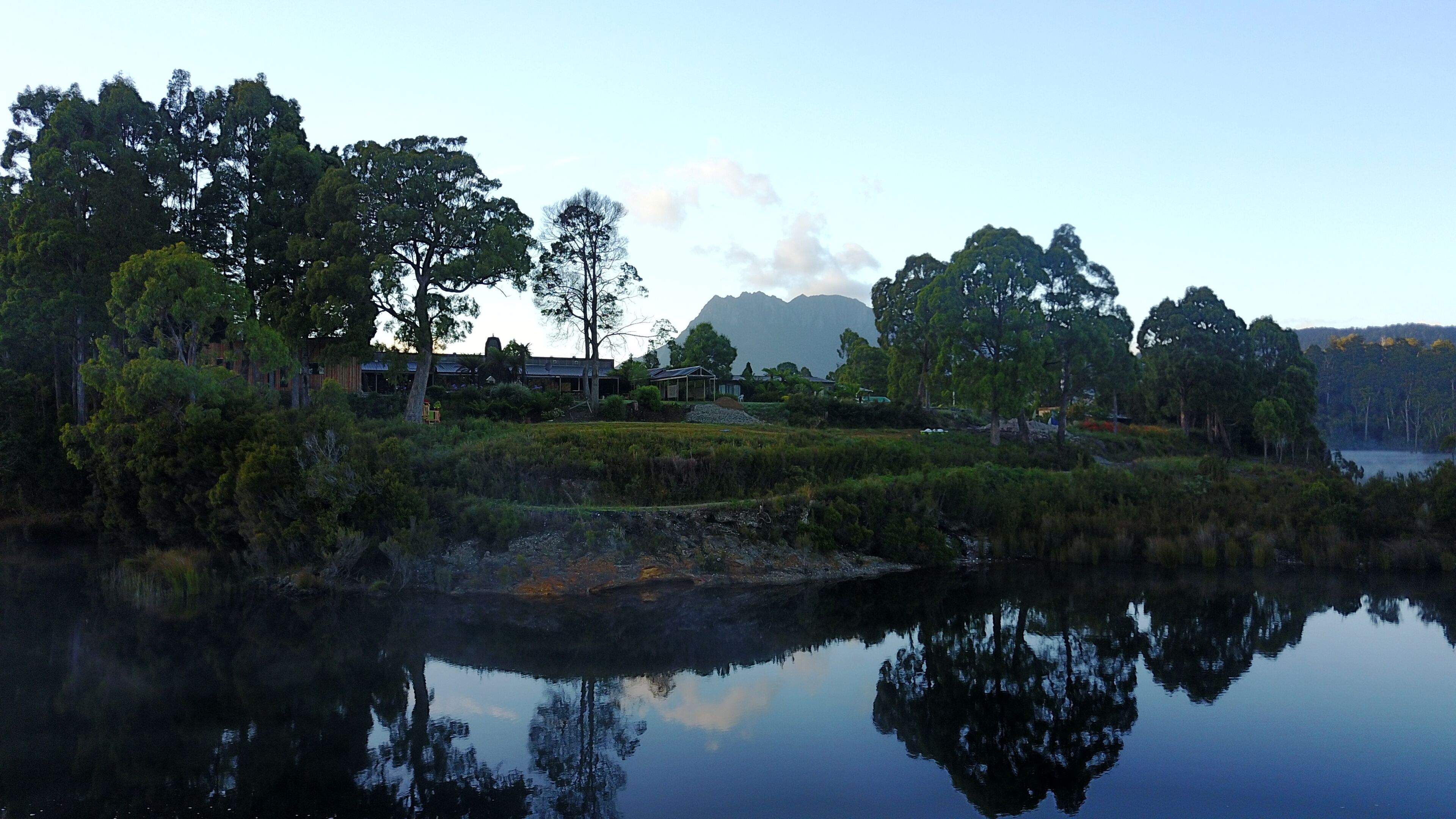 A lakeside property with a reflection of trees and a mountain in the background.