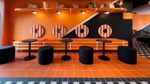 A modern lounge area with orange seating, black stools, and a checkered floor. - ibis Styles La Rochelle Centre les Minimes (La Rochelle)