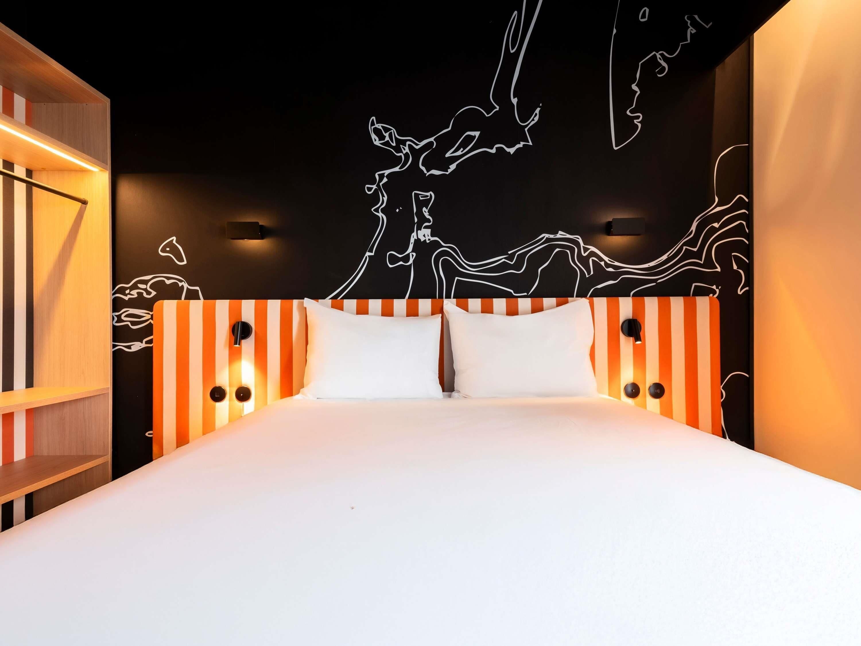 Une chambre d’hôtel moderne avec un grand lit, une tête de lit à rayures et une fresque murale.
