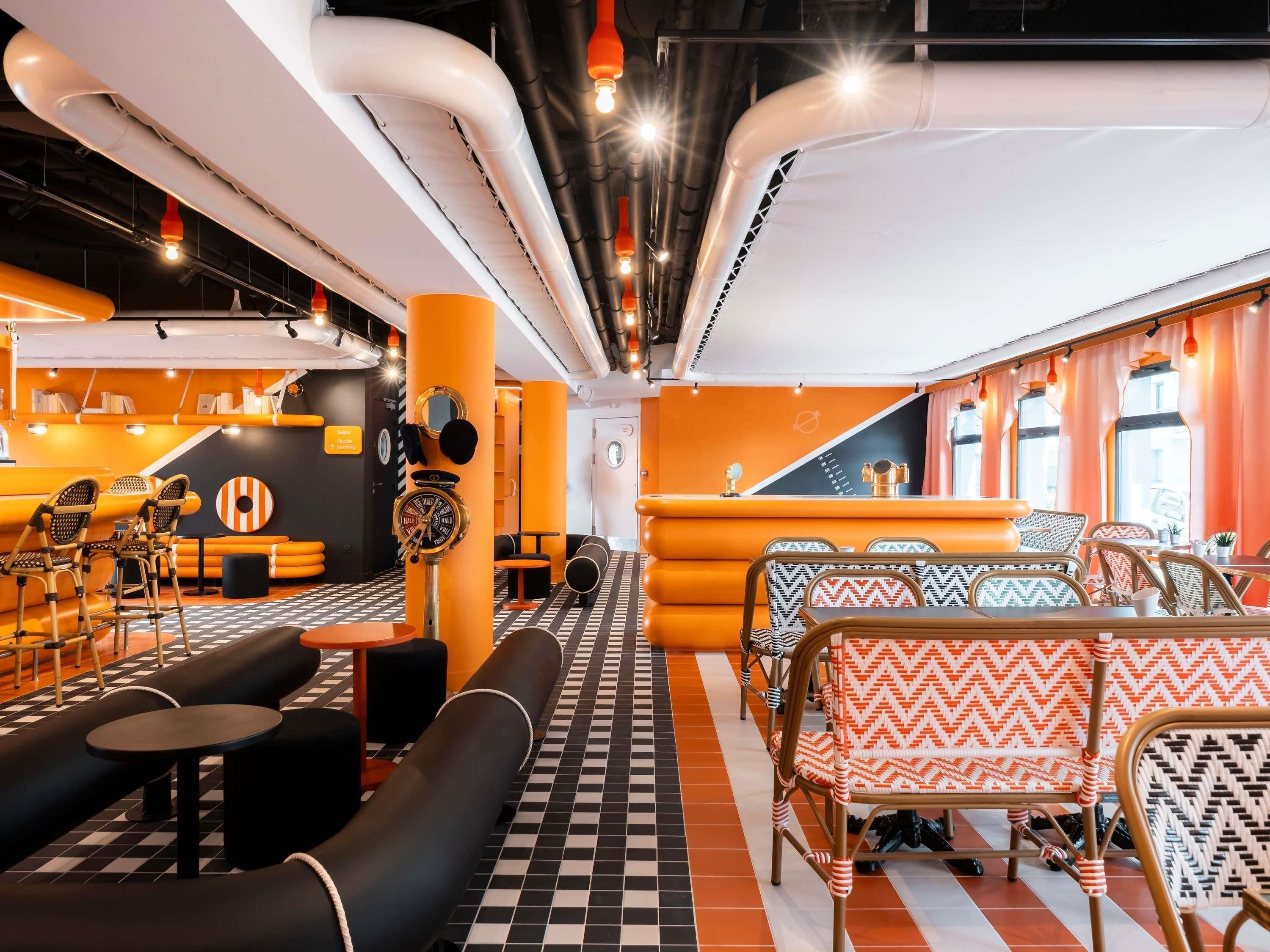 Un espace de détente moderne avec un sol à carreaux noirs et blancs, des murs orange et noirs, et une variété de sièges, notamment des canapés et des fauteuils à motifs.