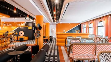 Un espace de détente moderne avec un sol à carreaux noirs et blancs, des murs orange et noirs, et une variété de sièges, notamment des canapés et des fauteuils à motifs.