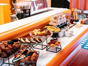 A buffet with various food items including bread, pastries, and a coffee machine. - ibis Styles La Rochelle Centre les Minimes (La Rochelle)