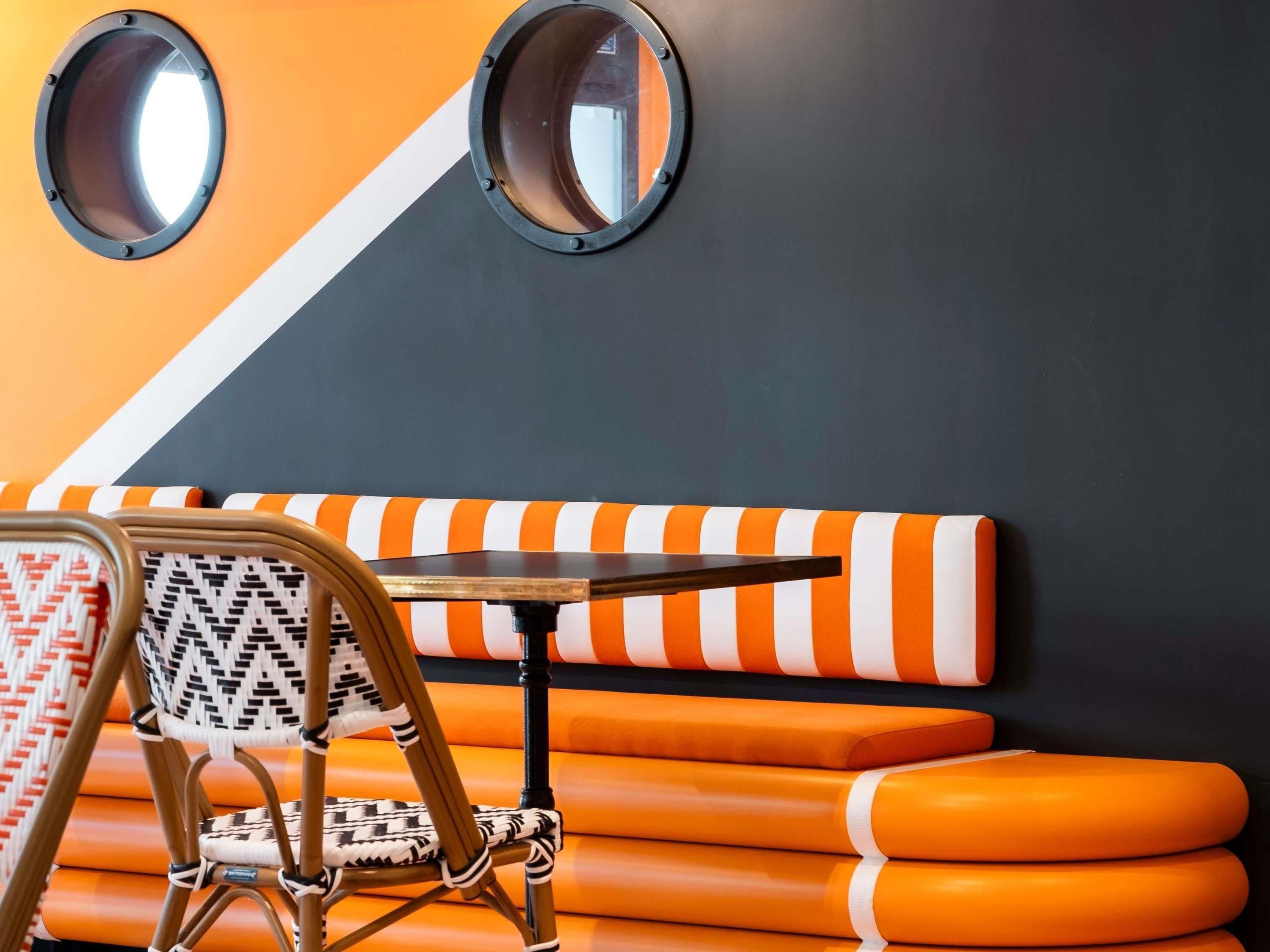 A seating area with a chair and a table, a wall with two circular mirrors, and orange and white striped cushions.