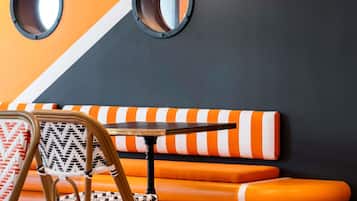 A seating area with a chair and a table, a wall with two circular mirrors, and orange and white striped cushions.